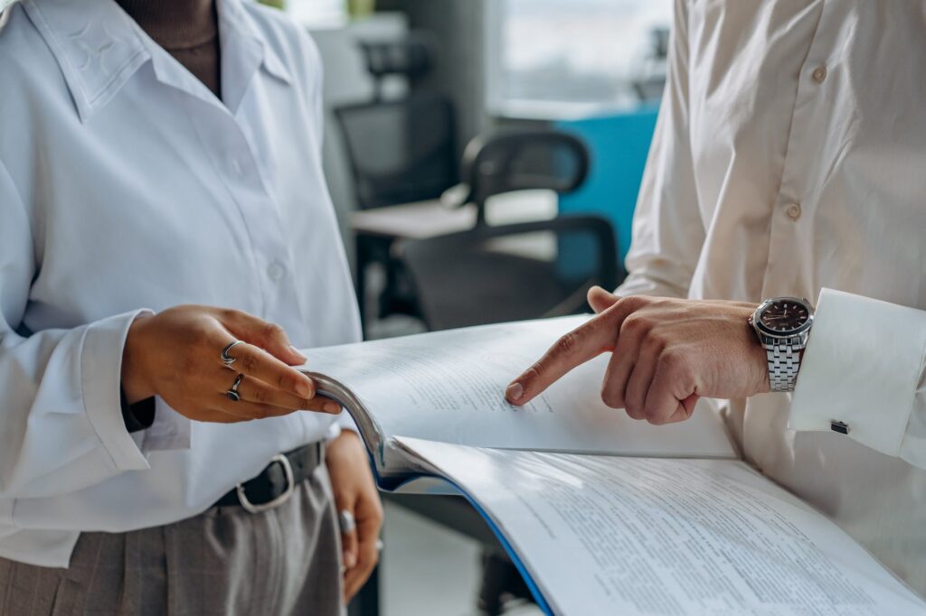 Cómo gestionar un negocio de forma exitosa 2 colleagues standing in white long sleeve shirts discussing and reading a financial report